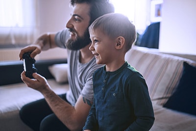 Un père et son jeune fils (4 ans) assis dans un canapé jouant aux jeux videos